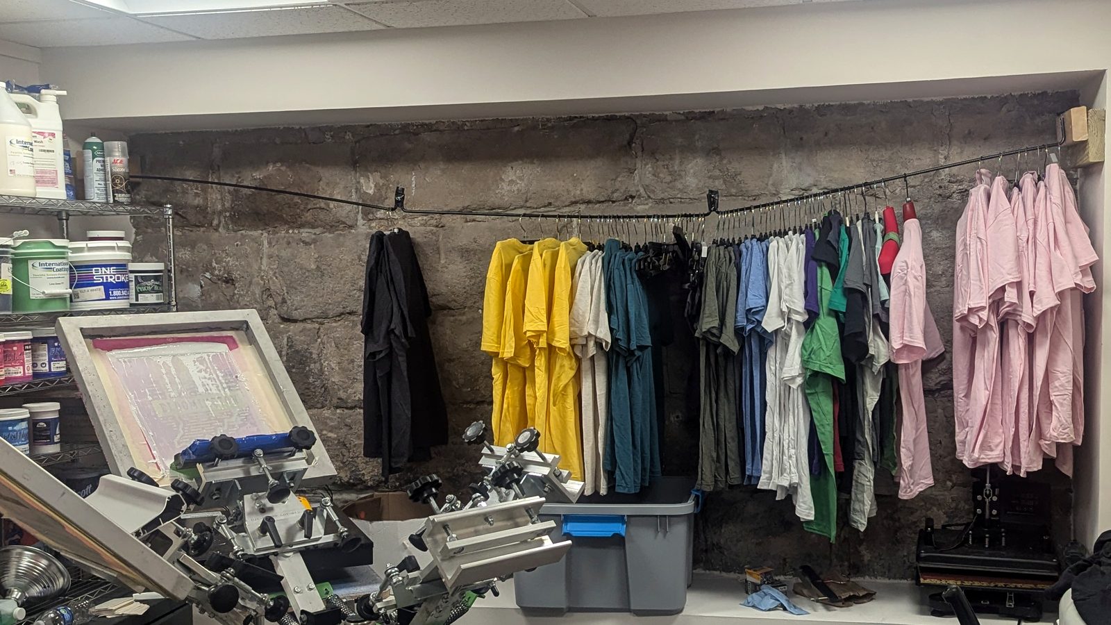 Inside the Retro Press shop: the press, ink on the shelves and a rack of printed shirts
